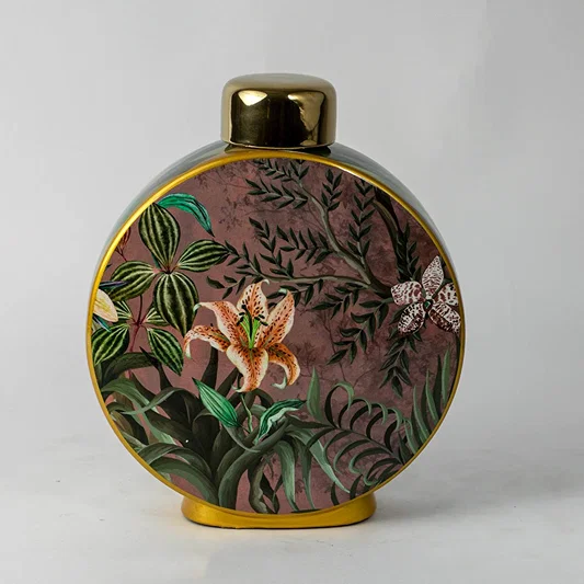 Round ceramic vase with tropical botanical artwork and gold neck placed on white surface against neutral background showcasing artistic modern home decor appeal.