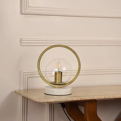Golden ring table lamp unlit on white background featuring glass globe and marble base suited for modern minimal home decor.