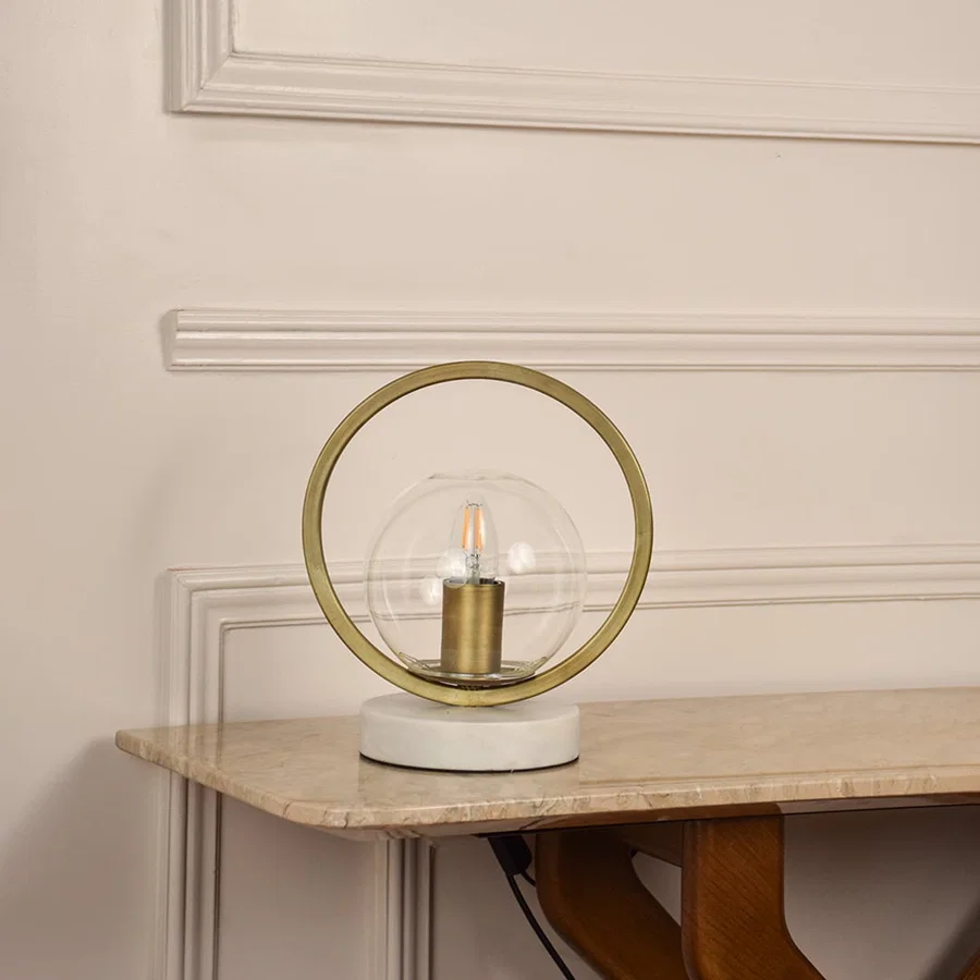 Golden ring table lamp unlit on white background featuring glass globe and marble base suited for modern minimal home decor.