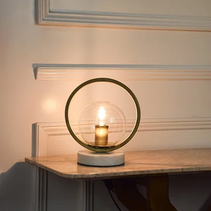 Circular metal table lamp with exposed bulb design creating warm ambient lighting for modern living spaces.