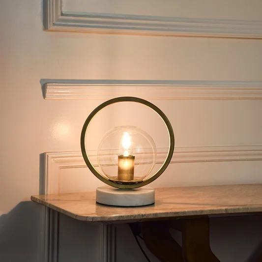 Circular metal table lamp with exposed bulb design creating warm ambient lighting for modern living spaces.