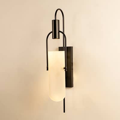 Black metal wall sconce with frosted glass shade glowing softly on white background for ambient lighting.