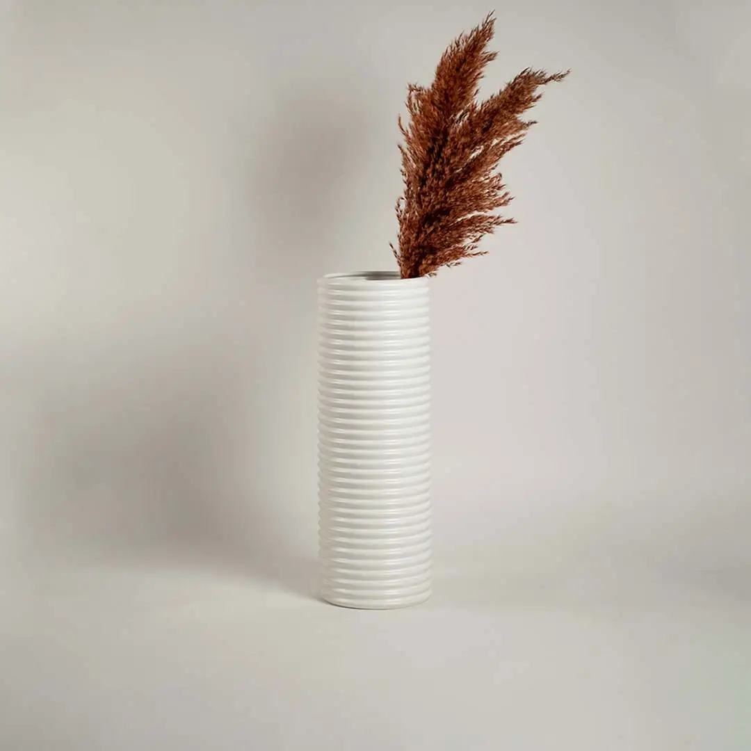 Glossy white cylindrical ceramic vase with linear ribbed design on white background reflecting minimal modern decor.