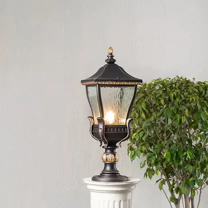 Elegant black and gold metal outdoor pillar light glowing with clear glass shade placed on decorative column lifestyle view.