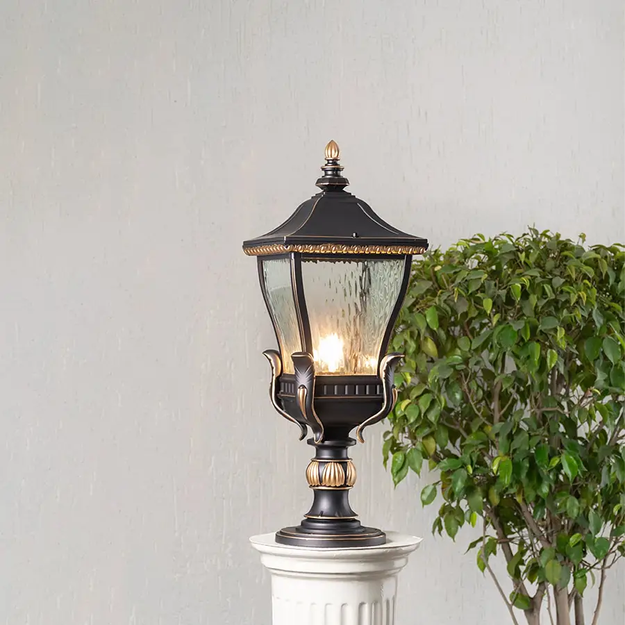 Elegant black and gold metal outdoor pillar light glowing with clear glass shade placed on decorative column lifestyle view.