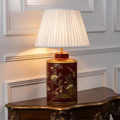 Light on white background features red ceramic table lamp illuminated to emphasize gold detailing floral motifs and warm light glow.