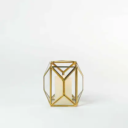 Gold metal and glass geometric lantern shown on a white background with candle on highlighting its modern structure and warm inviting glow.