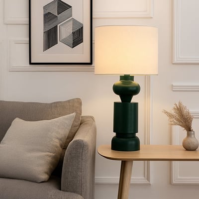 Dark green ceramic table lamp with cream shade styled in a cozy living room on a wooden side table beside a sofa.