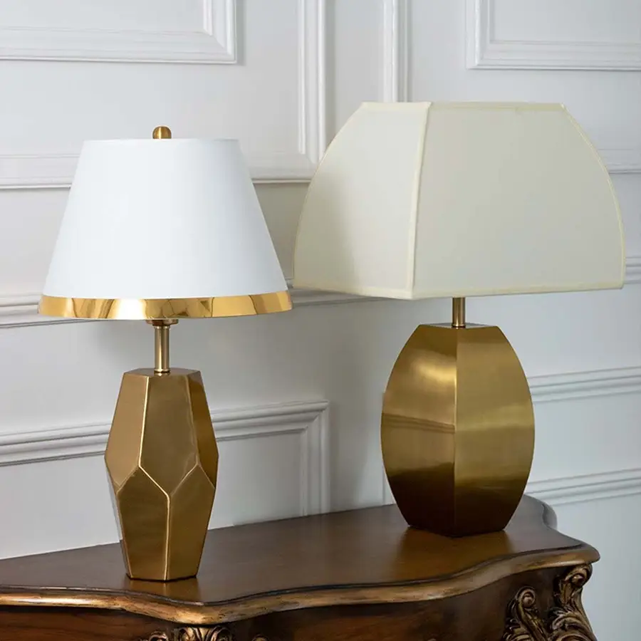 Gold faceted table lamps with white tapered shades shown together with lights off highlighting elegant geometric bases for modern home styling.