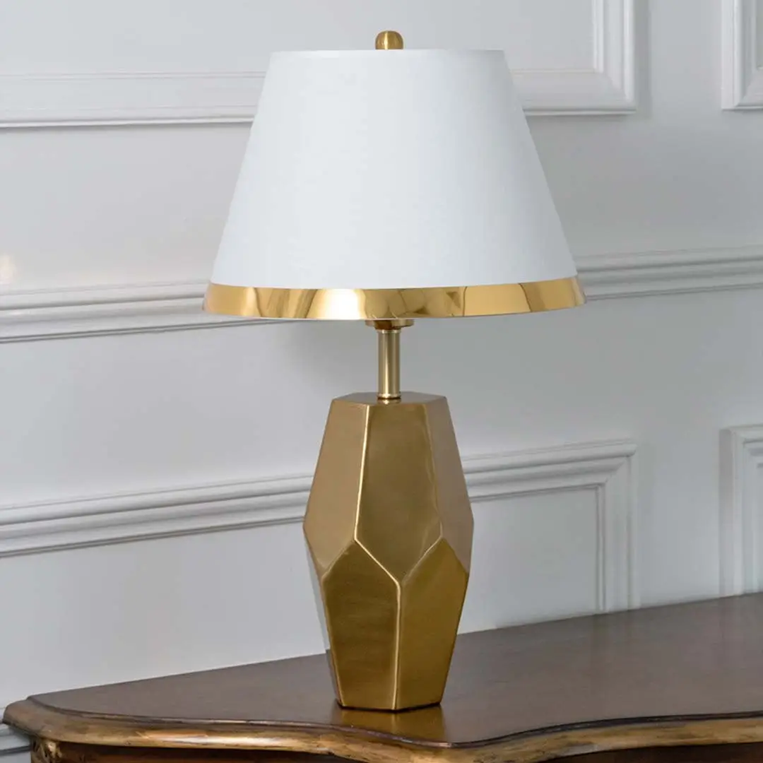 Gold faceted table lamp with white tapered shade and modern sculpted base displayed on a white background perfect for elegant interior styling.