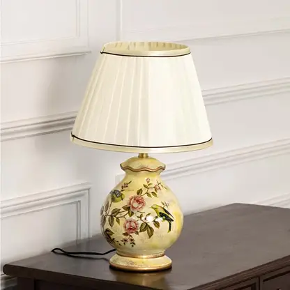 Unlit floral ceramic lamp with gold base and white pleated shade highlights its graceful silhouette and exquisite painted craftsmanship.