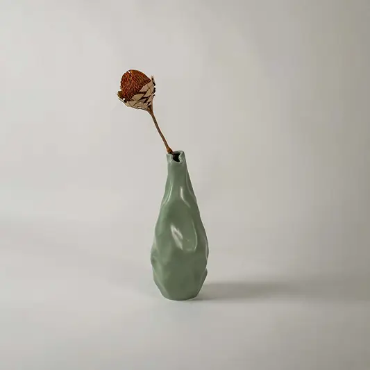 A modern green sculpted vase displayed in a soft lifestyle setting showing its unique organic shape and smooth artistic texture that enhances any contemporary decor.