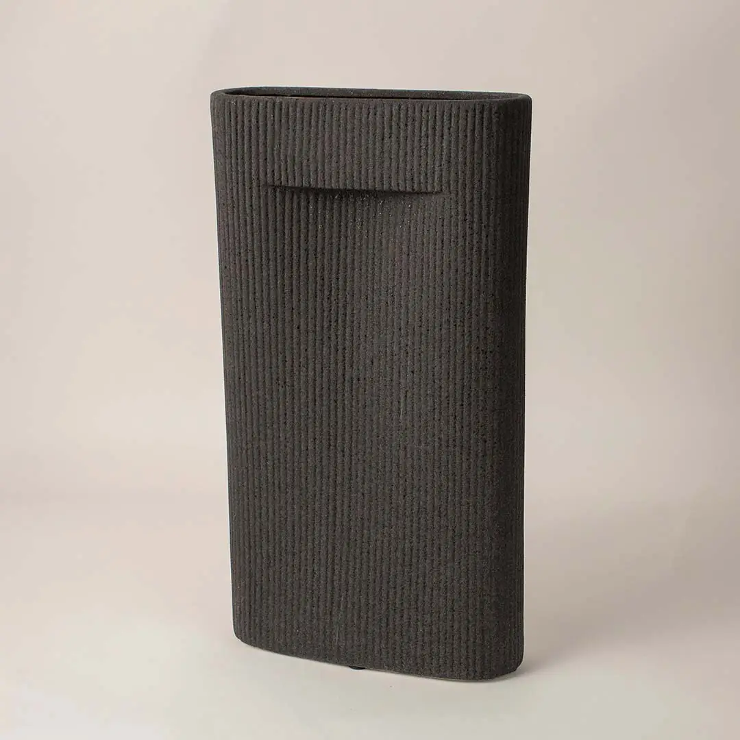 Ribbed black ceramic vase with soft matte finish placed side way showcasing its bold modern silhouette.