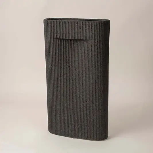 Ribbed black ceramic vase with soft matte finish placed side way showcasing its bold modern silhouette.