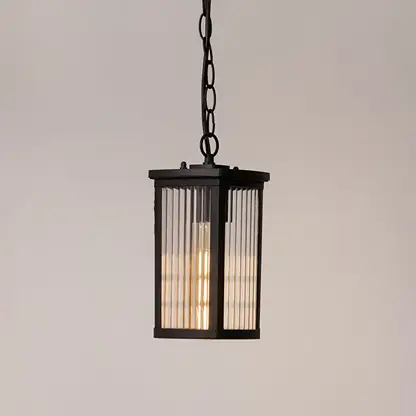 Black metal hanging lantern lit on white background highlighting warm glow and ribbed glass for home lighting.