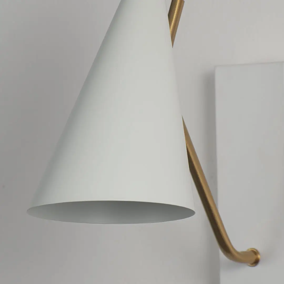 Elegant wall light with matte white conical shade and slim gold arm in closeup view highlighting minimal contemporary design.