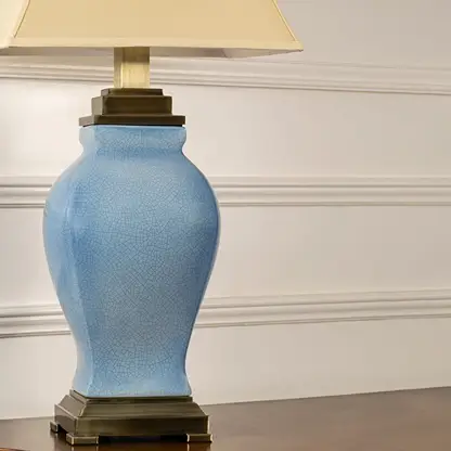 Closeup of cream shade blue ceramic table lamp on carved console table with light on and white panel wall background for classic elegant décor.