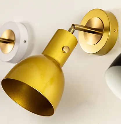 Gold wall light with a sleek metal shade mounted on a round base giving a modern warm focused glow suitable for hallways bedrooms or living spaces.