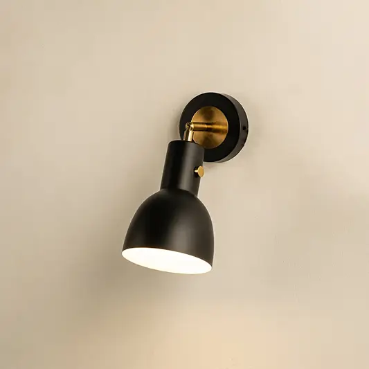 A matte black metal wall light shining warmly against a neutral beige wall adding focused lighting and modern functional sconce décor to interior spaces.