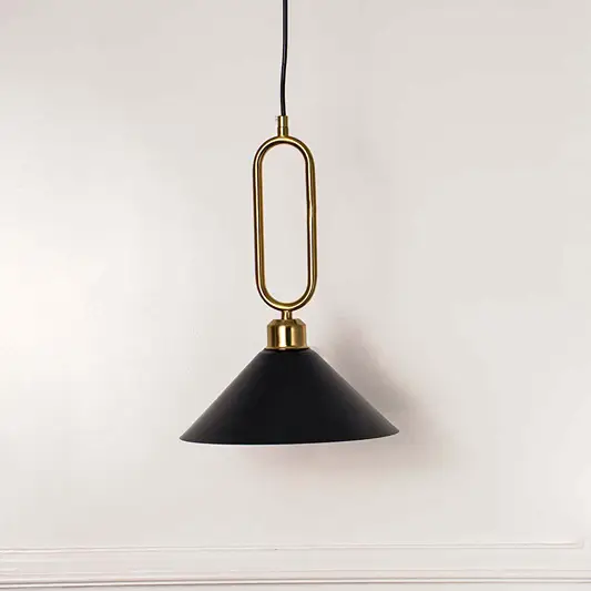 Modern black metal pendant light with gold loop handle and cone shade hanging against soft beige wall background for elegant interior decor lighting.