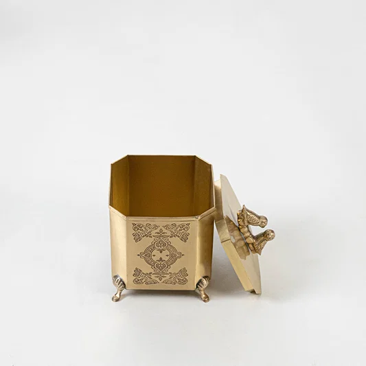 Decorative metal tissue box in gold finish with engraved design for dining table or decor accessory placement white background.