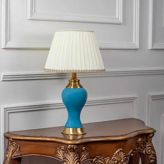 Blue ceramic table lamp turned off with pleated shade and golden base displayed on minimal white background.