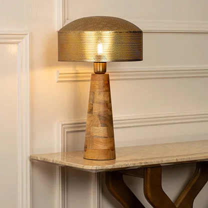 Gold metal table lamp with textured shade and natural wood base casting warm ambient light for luxury interior decor.
