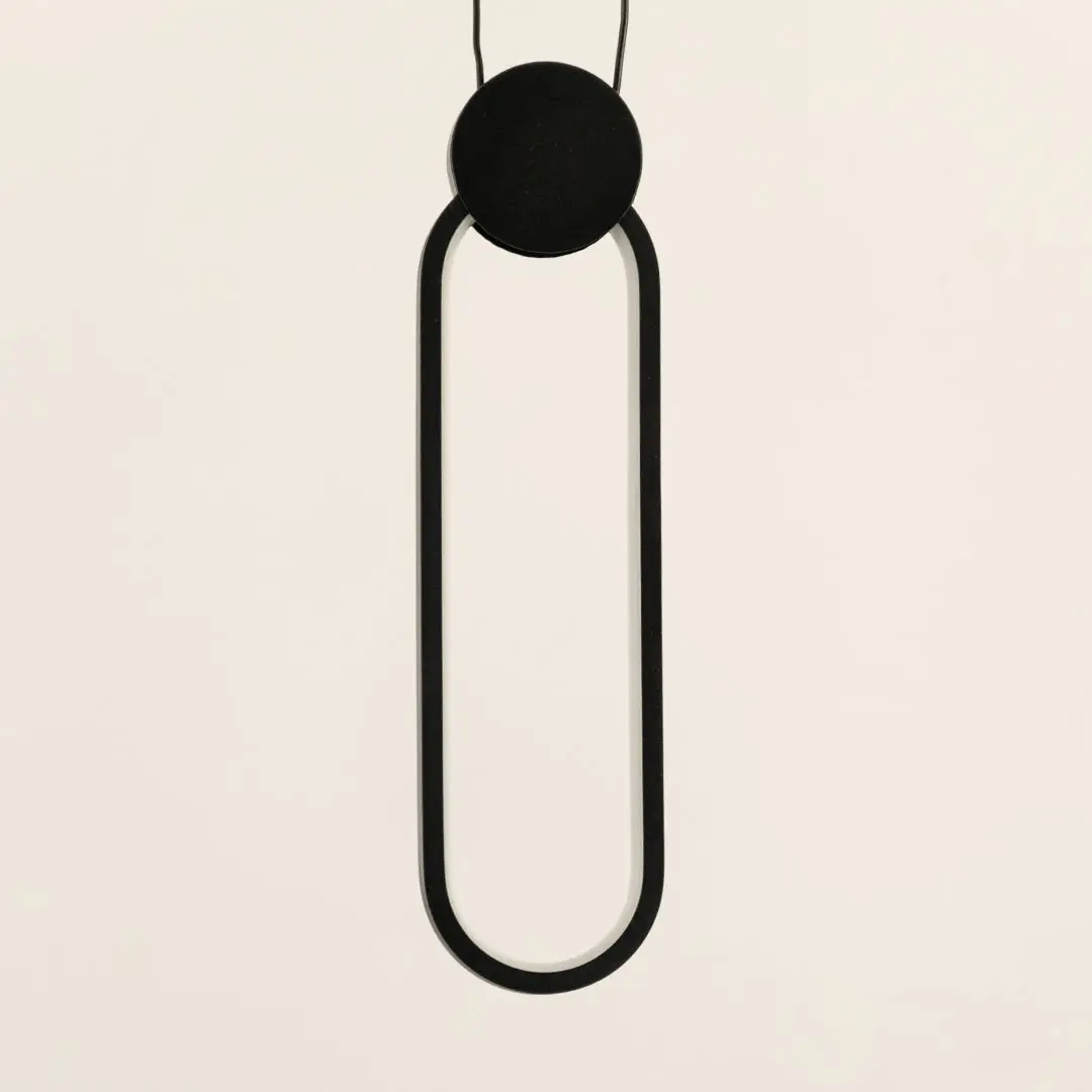 Minimal black pendant light with elongated oval frame and hanging cord placed against neutral wall background showcasing sleek contemporary lighting decor aesthetic.