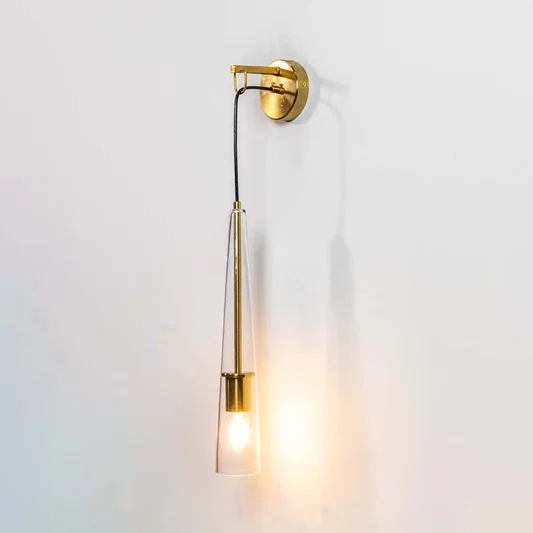Minimalist gold brass long slim arm wall sconce casting a bright warm ambient light setup isolated on a white backdrop.