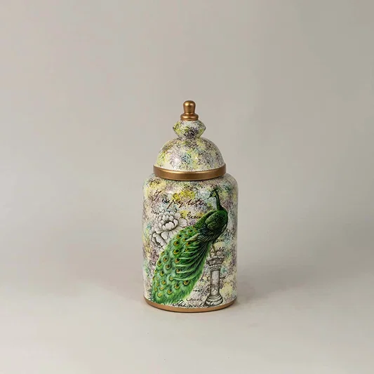 Ceramic jar with green parrot and botanical artwork and gold lid placed on white surface against neutral background enhancing elegant artistic home decor styling.