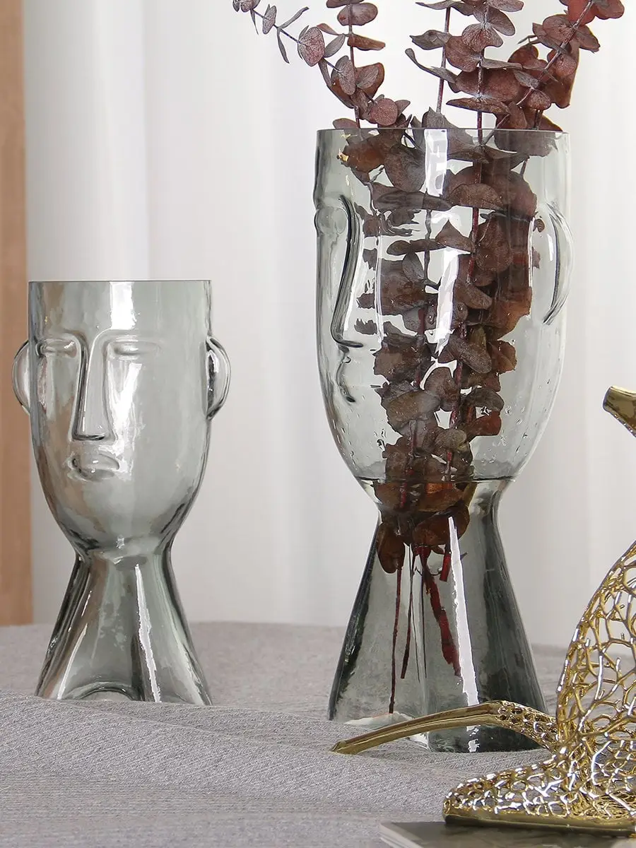 Set of face shaped glass vases in clear finish styled with dry branches modern artistic decor for living room and tabletop styling.