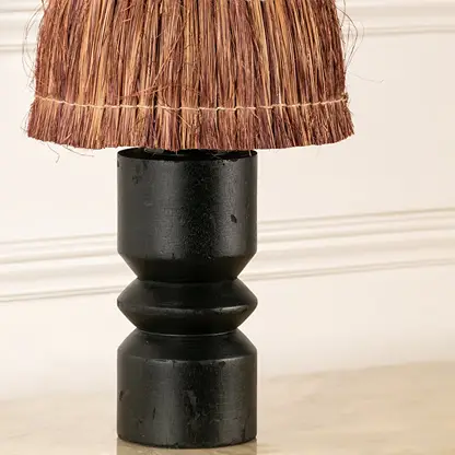 Woven brown fiber lamp shade with black wood base highlighting handcrafted texture and decorative craftsmanship.