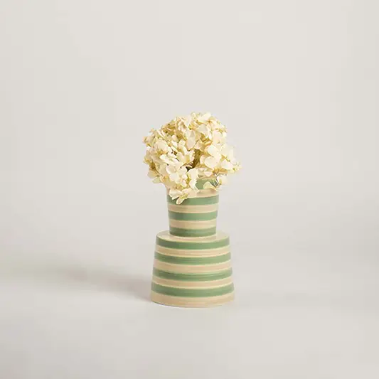 Contemporary striped ceramic vase in green and beige set on a plain white backdrop  emphasizing its modern shape and decorative appeal.