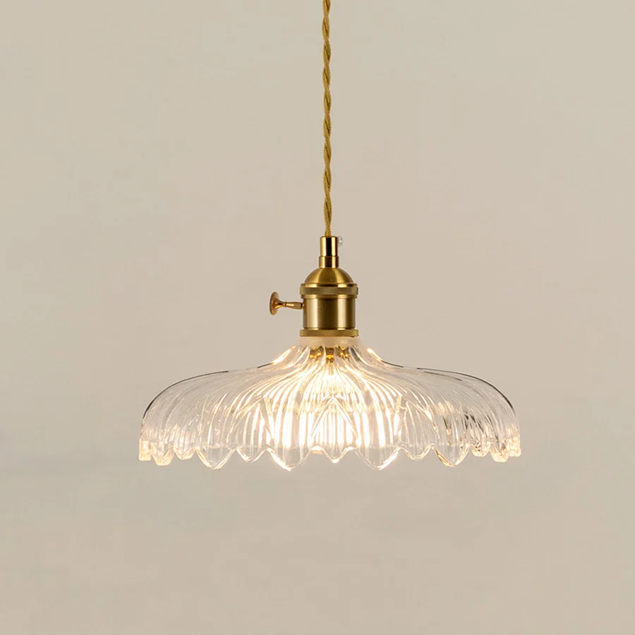 Illuminated clear patterned glass pendant light with gold fittings creating soft ambient lighting indoors.