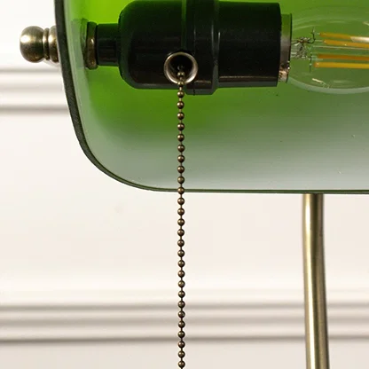 Macro shot of brass base and green glass top of banker table lamp revealing elegant texture and vintage finish.