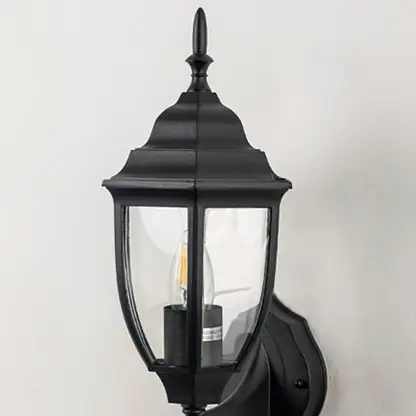 Closeup image of black metal outdoor wall light with clear glass shade for stylish exterior decor.