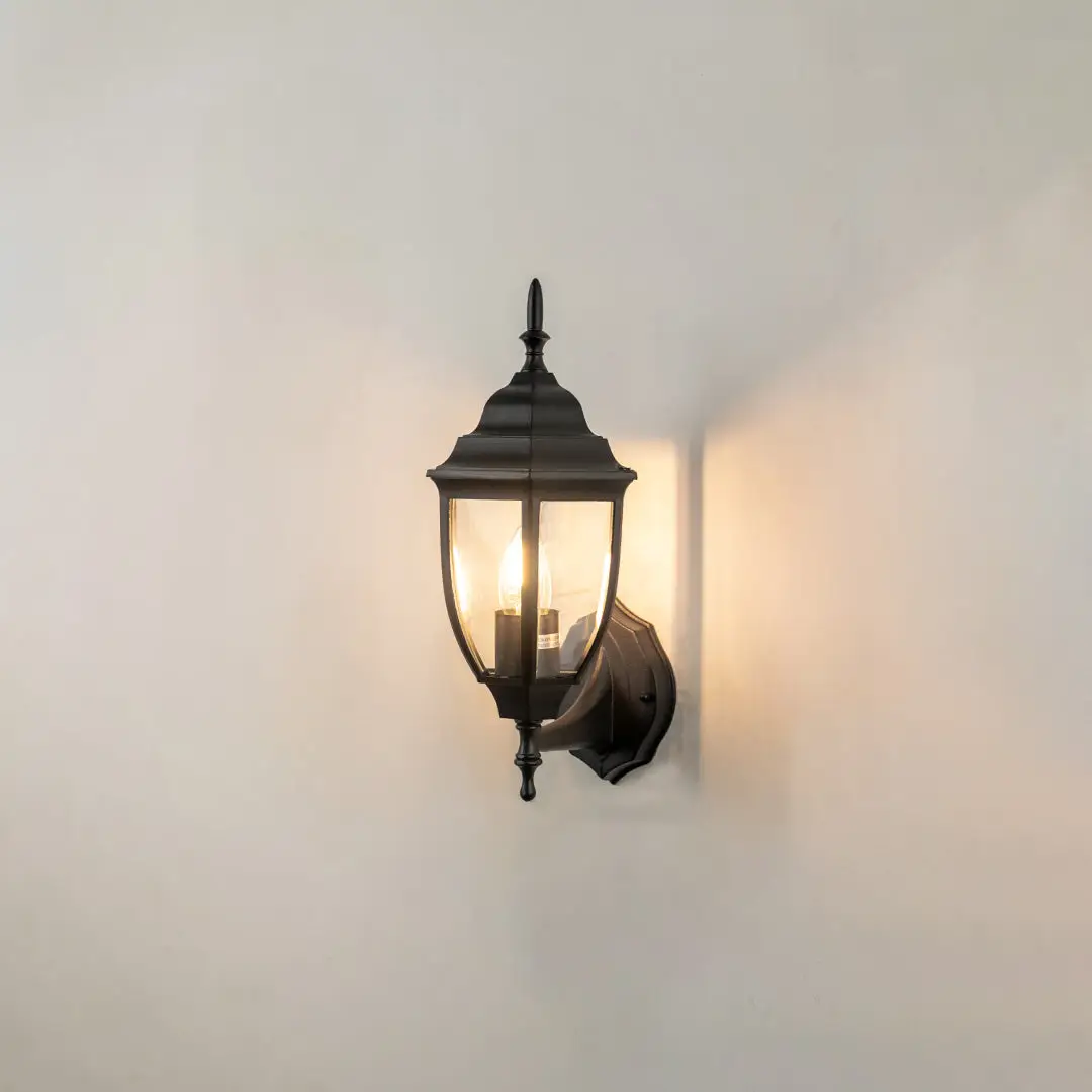 Black metal outdoor lantern wall light on white background with warm glow for classic patio decor.