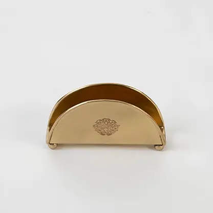 Half-round brass napkin holder with floral crest placed on white background showcasing finish and elegant shape.