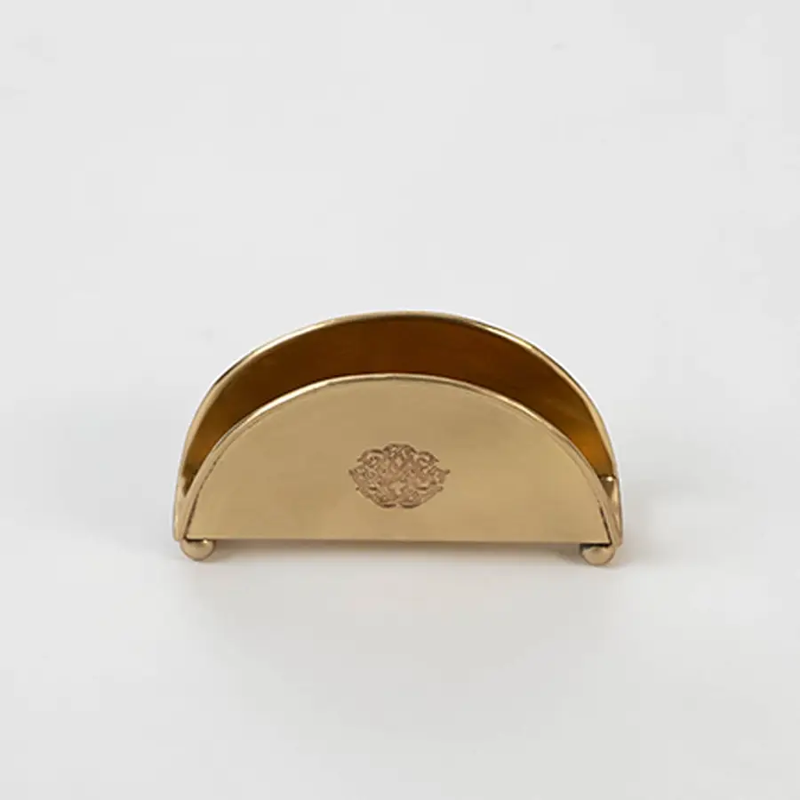 Half-round brass napkin holder with floral crest placed on white background showcasing finish and elegant shape.