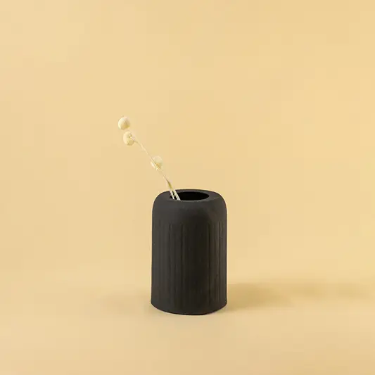 Minimalist matte black cylindrical vase with single dried bud for chic modern home decor and shelf display style.