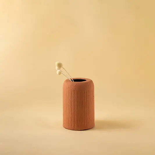 Minimalist terracotta metal cylindrical vase with dried flower bud for elegant home decor and shelf style.