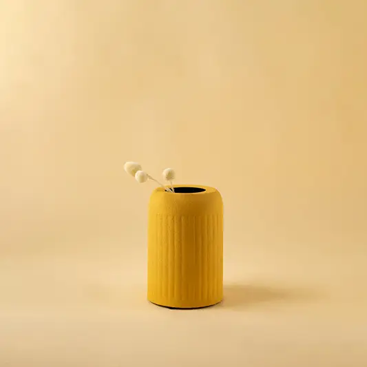 Small yellow metal cylindrical vase with dried flower bud for minimalist home decor and modern table accents.