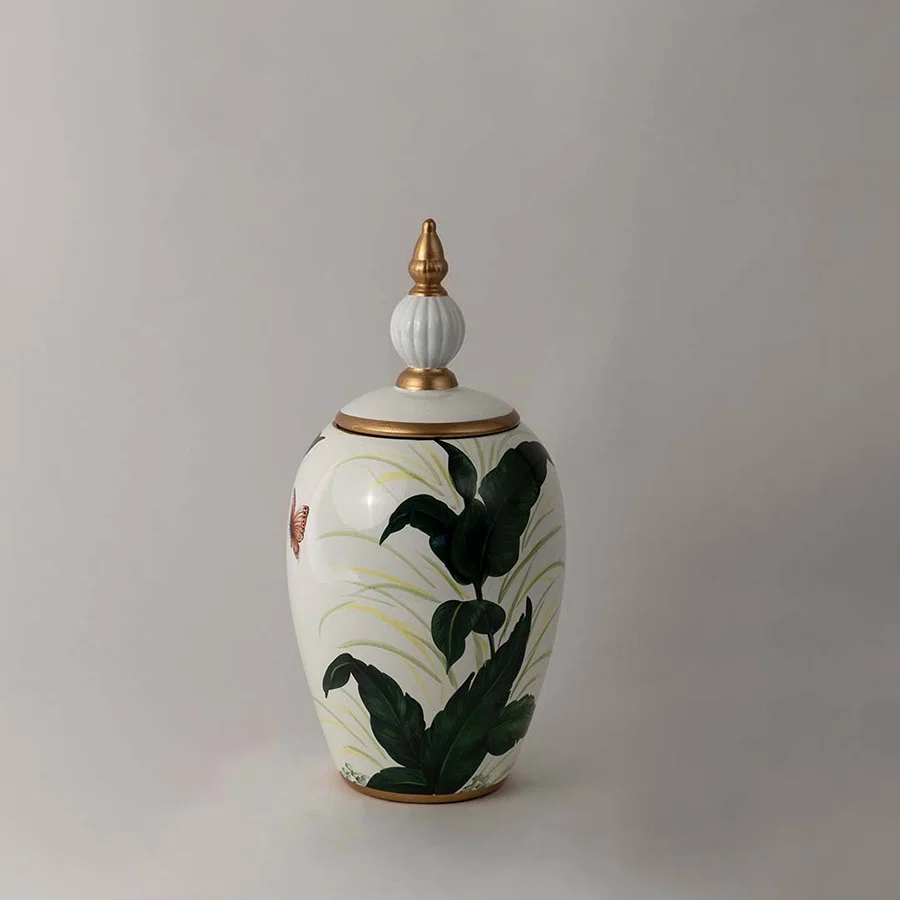 Decorative ceramic jar with green botanical leaf artwork and gold lid placed on white surface against neutral background showcasing elegant modern home decor styling.