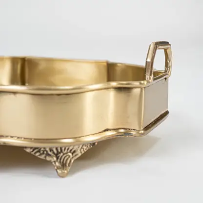A closeup view of the ornate golden serving tray showing its intricate carved border smooth surface and elevated feet that enhance its premium handcrafted appearance.