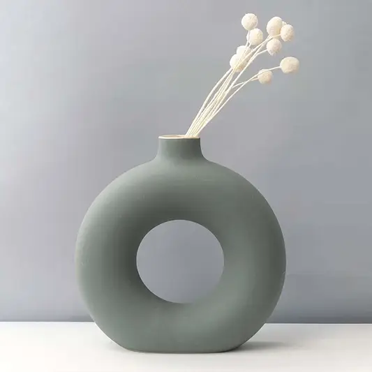 Grey round ceramic vase with hole design styled with white dried flower stems modern home decor accent for table.