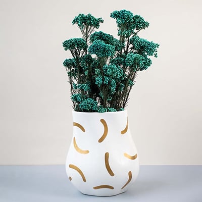 Green dried statice flower stems arranged in modern white ceramic vase with gold patterns elegant lifestyle decor.