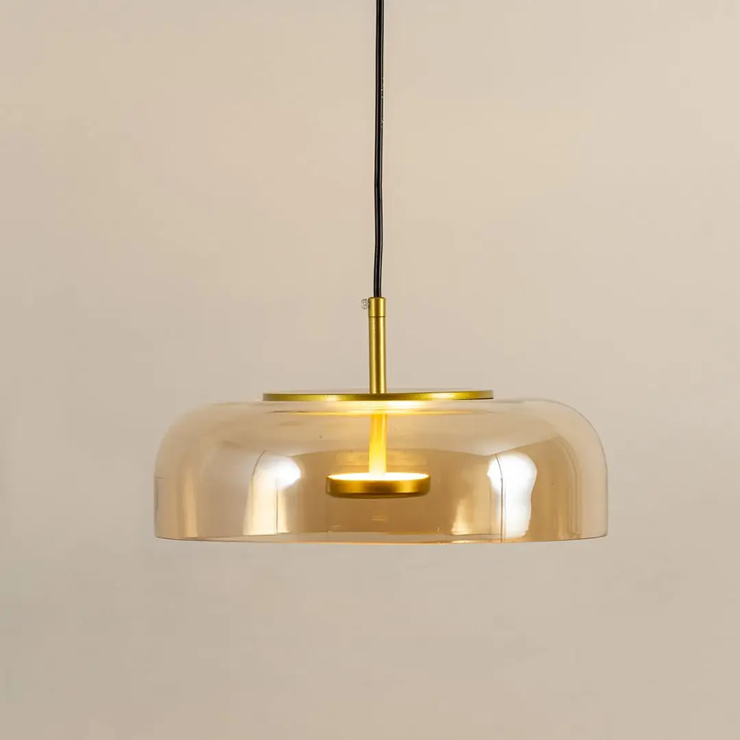 Amber glass pendant light with gold metal fixture illuminated to display luxury decorative ceiling lighting elegance.