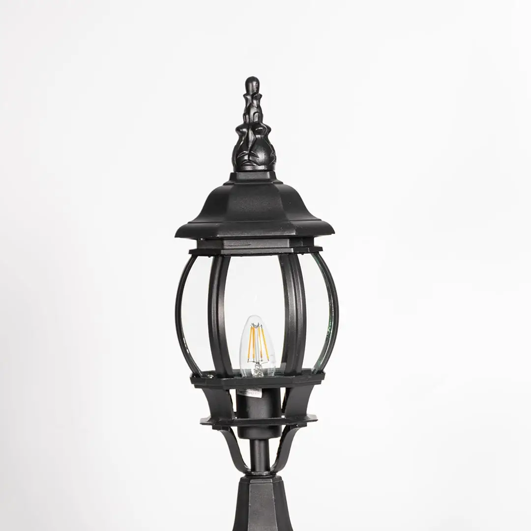 Closeup of decorative tall outdoor black pillar lamp with curved round glass panels and LED bulb showing vintage style.
