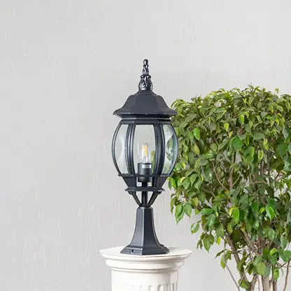 Classic tall black outdoor pillar lamp with clear round glass shade placed on stone pillar ideal for villa garden entrance.