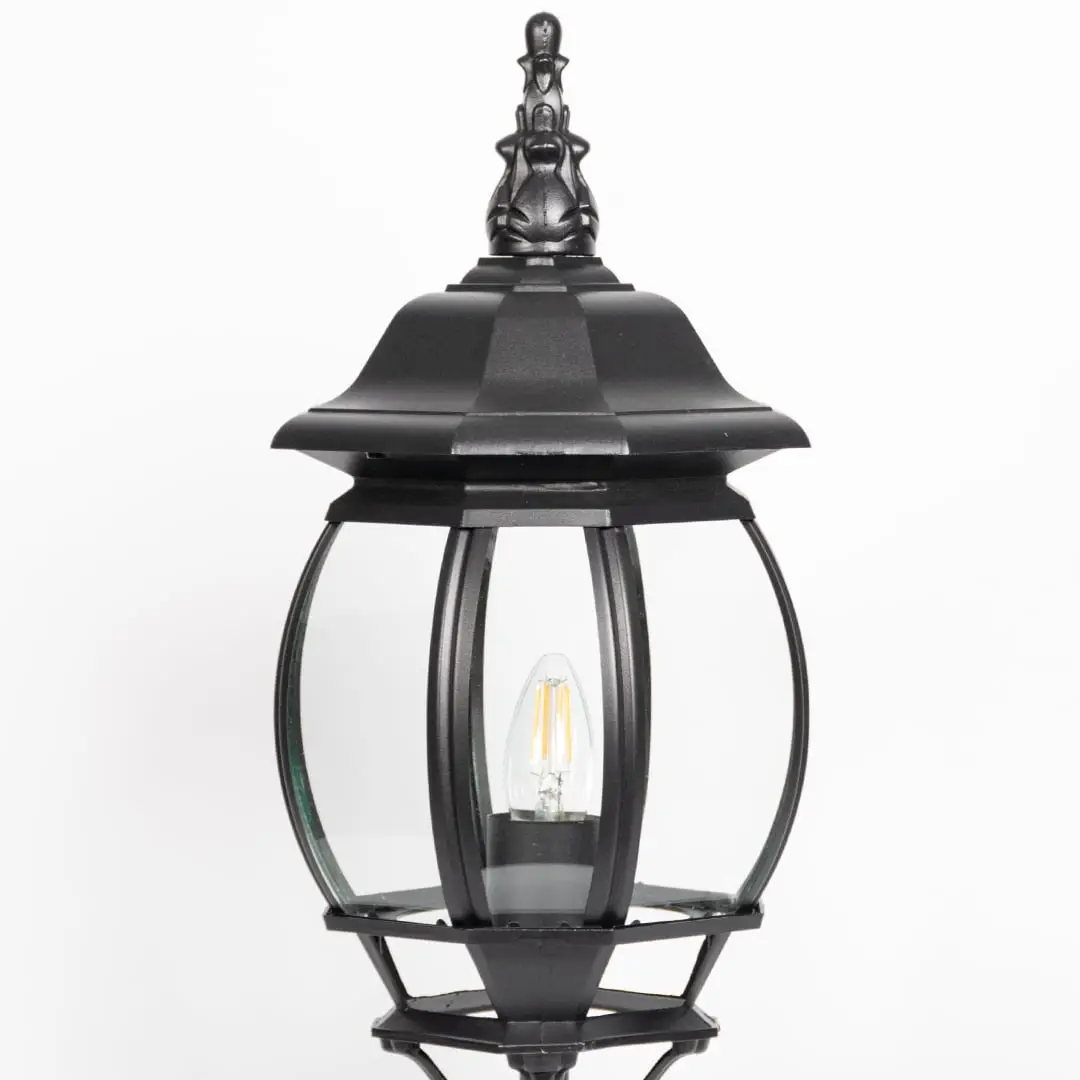 Closeup of decorative black pillar light with curved glass panels and LED bulb showcasing elegant outdoor lighting.
